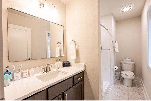 A bathroom with a large mirror, a sink with toiletries, a toilet, and a shower area.