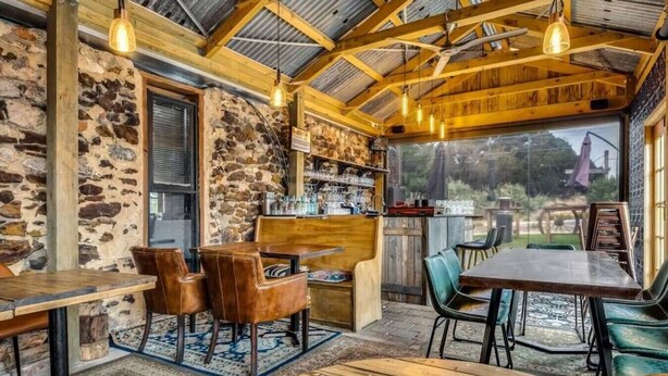 A rustic interior with stone walls, wooden beams, and a bar area with stools and a table.