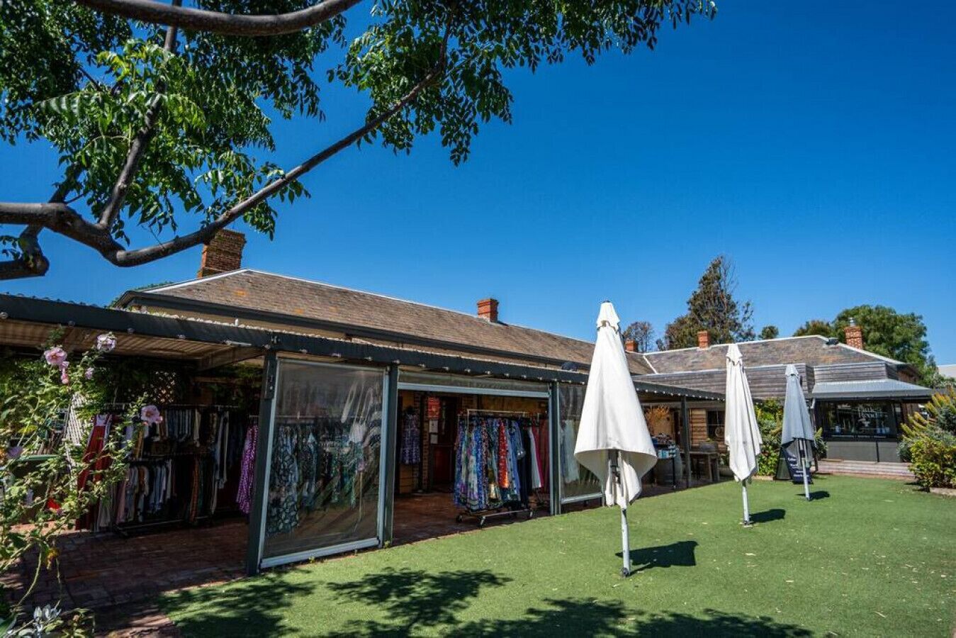 A boutique hotel with a covered outdoor seating area, a shop with colorful fabrics, and a well-maintained lawn.