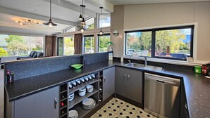 Una cocina moderna con encimeras oscuras, electrodomésticos de acero inoxidable y abundante luz natural gracias a amplias ventanas.