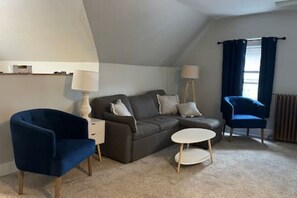 Et hyggeligt rum med sofa, to stole, et lille bord og en lampe.