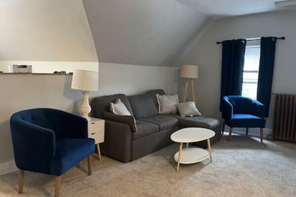 Ein gemĂŒtliches Zimmer mit einer Couch, zwei Sesseln, einem kleinen Tisch und einer Lampe.
