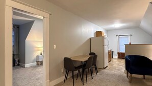 A spacious room with a dining table and chairs, a small kitchen area, and a dark blue chair. - NH3 - Historic Charm - Cozy 3BR Apartment (DuBois)