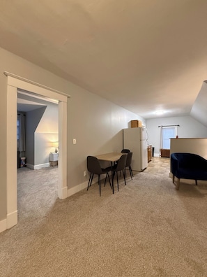 A spacious room with a dining table and chairs, a small kitchen area, and a dark blue chair.