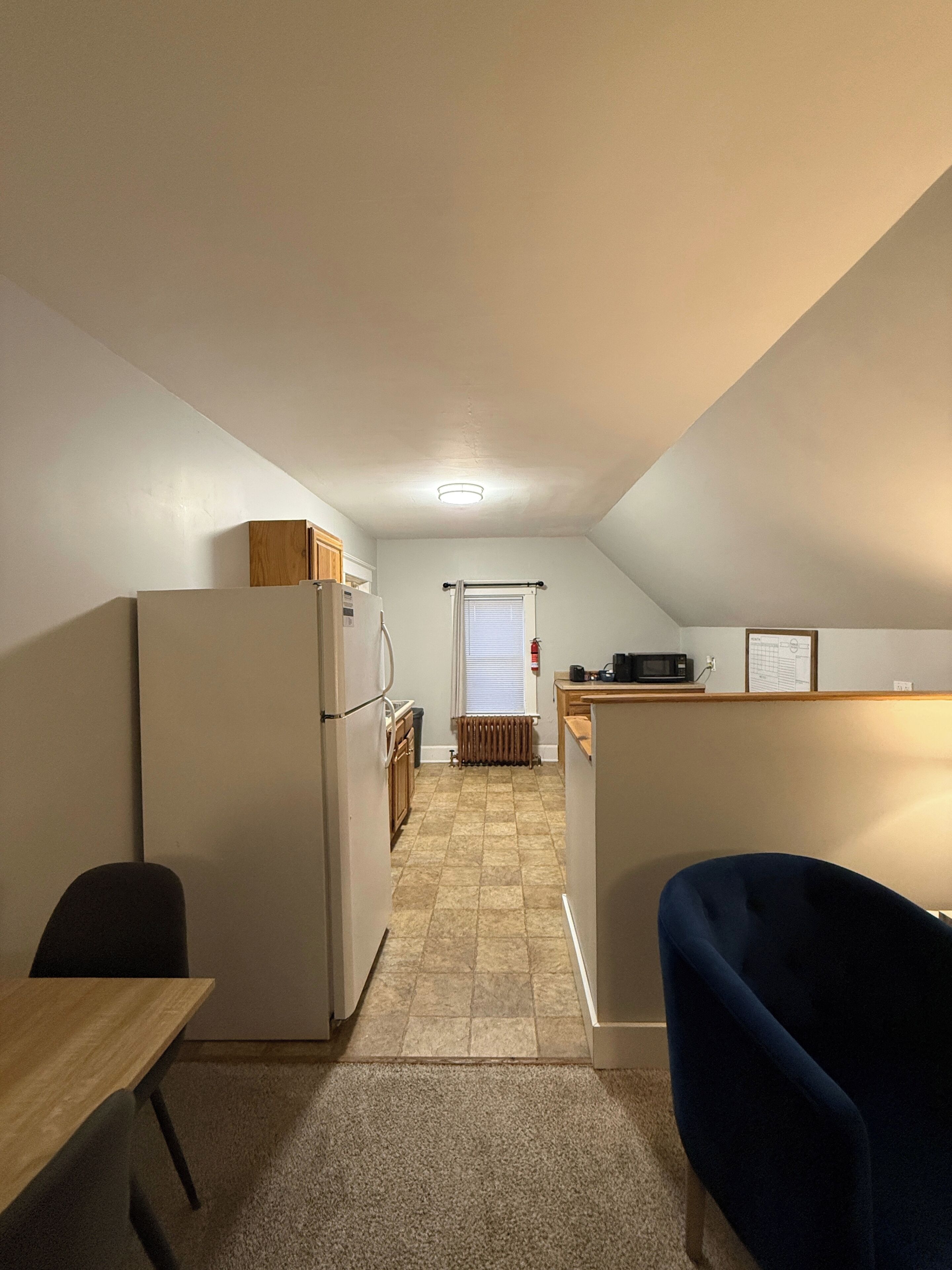 A compact kitchen with a refrigerator, microwave, and a window with blinds.