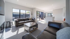 Een moderne woonkamer met een bank, salontafel en uitzicht op de achtertuin door grote schuifdeuren.