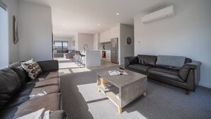 Een moderne woonkamer met een bank, een salontafel en een zithoek. Achtergrond is een keuken met een koelkast en een spoelbak.