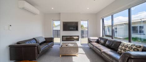 A modern living room with a grey carpet, two leather sofas, a coffee table, and a flat-screen TV mounted on the wall.