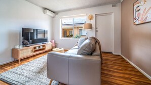 Una sala de estar moderna con sofá, televisor y ventana con vistas a una casa.