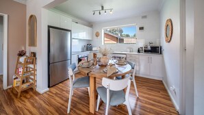 Una cocina moderna con armarios blancos, un refrigerador de acero inoxidable y un comedor con mesa y sillas de madera.