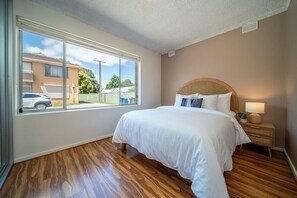 A bedroom with a large window, a bed with white bedding, a wicker headboard, and a bedside table with a lamp. - Casa Boho—Peaceful Stay in Vibrant, Central Locale (Everard Park)