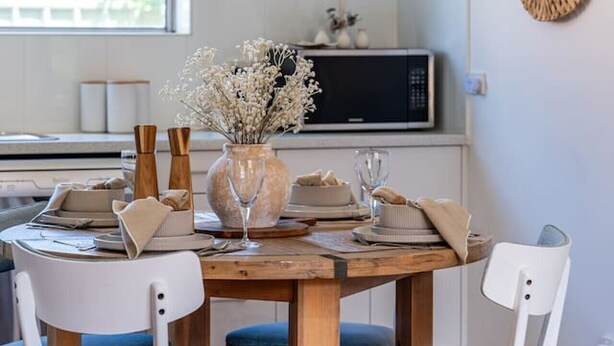 Un comedor con una mesa de madera, sillas blancas y un jarrón con flores.