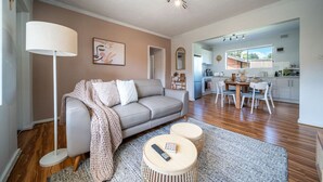 Una sala de estar moderna con sofá, mesa de centro y lámpara. Se ve un área de cocina a través de una puerta abierta.