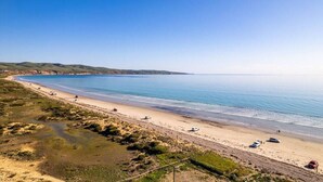 Une plage côtière offrant une vue dégagée sur la mer, avec un rivage sablonneux et des collines à l’horizon.