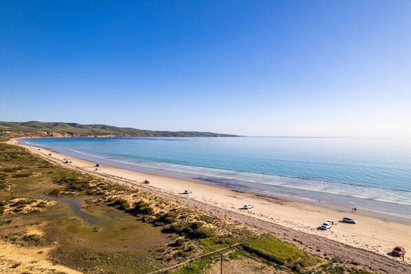 A coastal beach with a clear view of the sea, sandy shore, and distant hills.