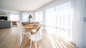 Une salle à manger lumineuse avec une table en bois, des chaises blanches et un lustre.