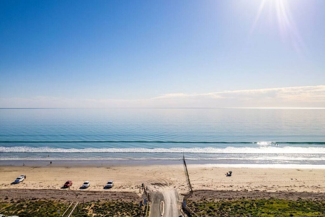 Une plage avec un ciel dégagé, une mer calme et une route menant au rivage.