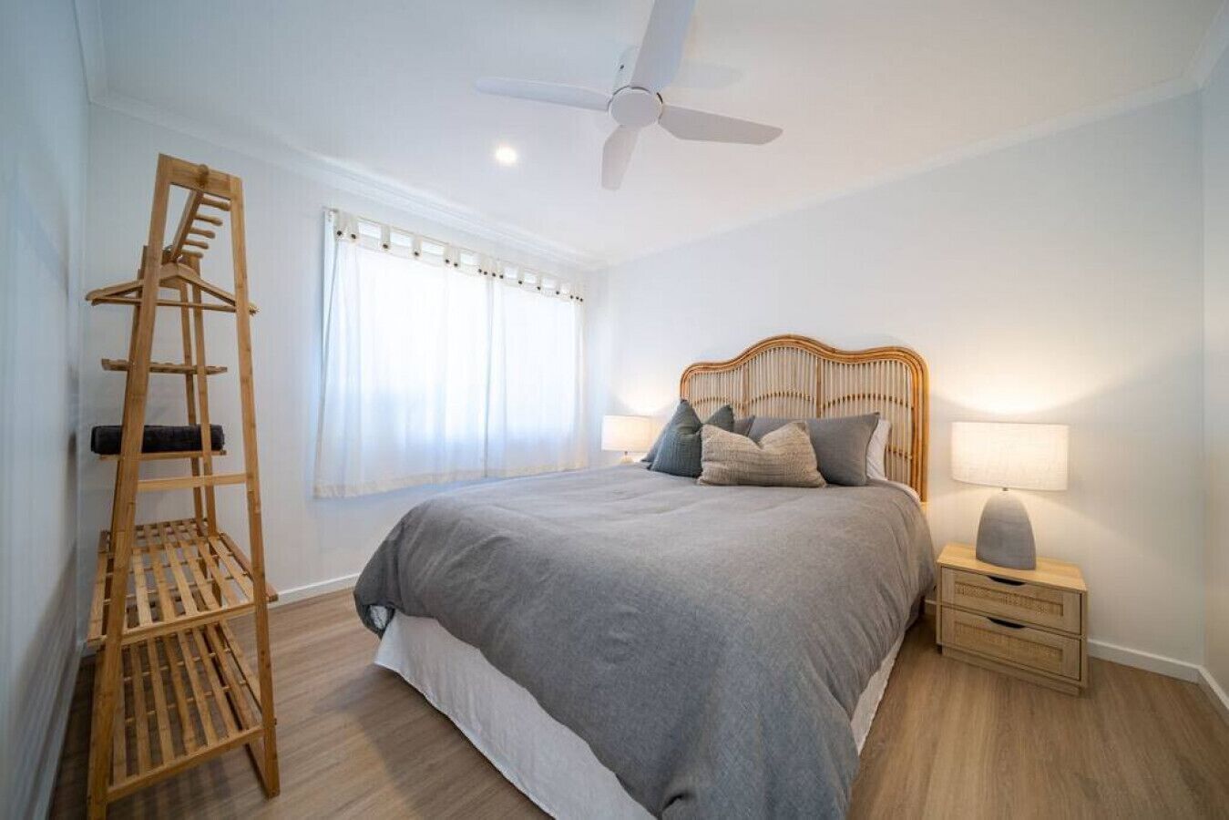 A bedroom with a bed, a wooden ladder, a ceiling fan, a nightstand with a lamp, and a window with curtains.
