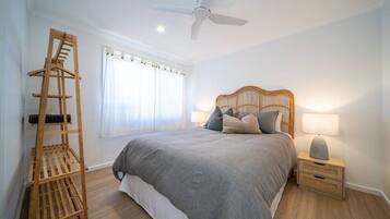 A bedroom with a bed, a wooden ladder, a ceiling fan, a nightstand with a lamp, and a window with curtains.
