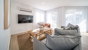 Un salon moderne avec un téléviseur à écran plat, une table basse en bois, un canapé confortable et des rideaux légers.