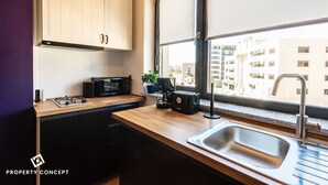 Une cuisine moderne dotée d’un plan de travail en bois, de meubles noirs, d’un four à micro-ondes encastré, d’une machine à café et d’une fenêtre donnant sur des immeubles.