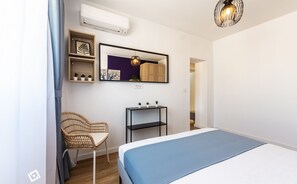 Ein Schlafzimmer mit einem Bett, einem Sessel, einem kleinen Tisch mit Pflanzen, einem Spiegel und einer Pendelleuchte.