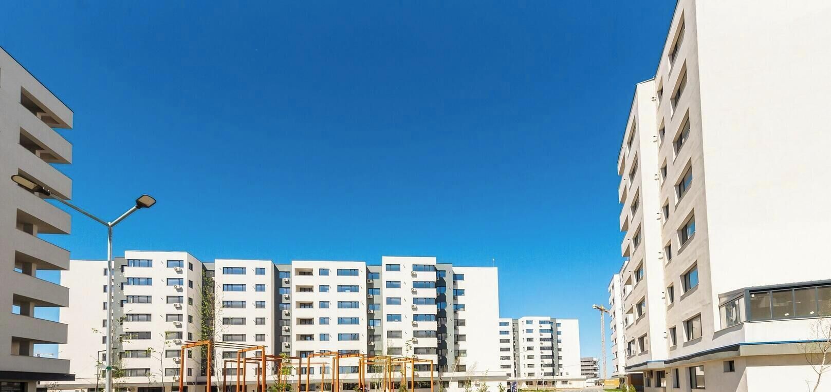 Una strada cittadina moderna con edifici residenziali a più piani, cielo sereno e un attraversamento pedonale.