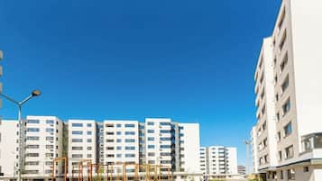 Una strada cittadina moderna con edifici residenziali a più piani, cielo sereno e un attraversamento pedonale.