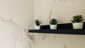 A bathroom with white marble tiles and a black shelf holding three potted plants. - Elegant Apartment in Ivory - AC and Smart TV (Voluntari)