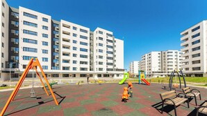 A playground with swings and slides, surrounded by apartment buildings. - Elegant Apartment in Ivory - AC and Smart TV (Voluntari)