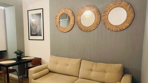 A living room with a beige sofa, a dining table with chairs, and three wall-mounted mirrors. - Elegant Apartment in Ivory - AC and Smart TV (Voluntari)