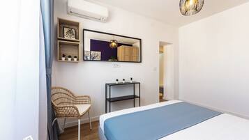 A bedroom with a bed, a chair, a shelf with plants, a mirror, and an air conditioner.