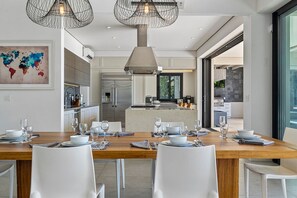 Eine moderne Küche mit Kochinsel, Edelstahlgeräten und einem Essbereich mit weißen Stühlen und einem Holztisch für sechs Personen.