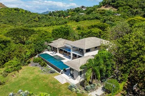Ein modernes, zweistöckiges Haus mit Schwimmbad, umgeben von üppiger Vegetation und Hügeln.
