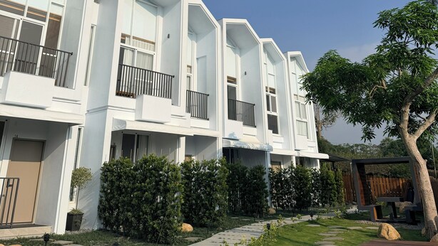 A modern multi-story residential building with balconies, a well-maintained garden, and a clear blue sky. - KUMOYOKU B&B (Taichung)