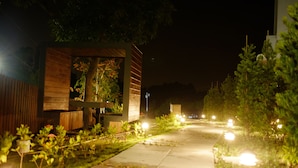 A nighttime pathway flanked by greenery and illuminated by street lamps, leading to a modern building with a wooden facade and a visible window. - KUMOYOKU B&B (Taichung)
