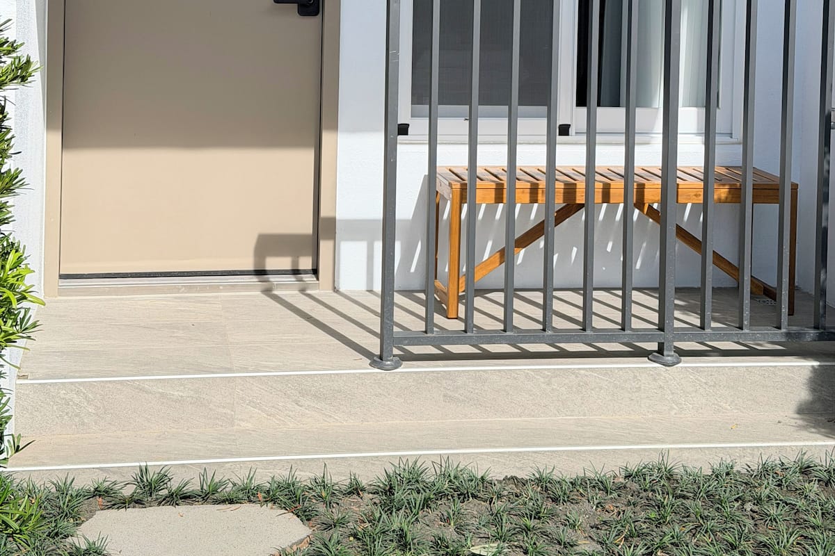 A door labeled "1B" with a small wooden table and a metal railing in front of a window.