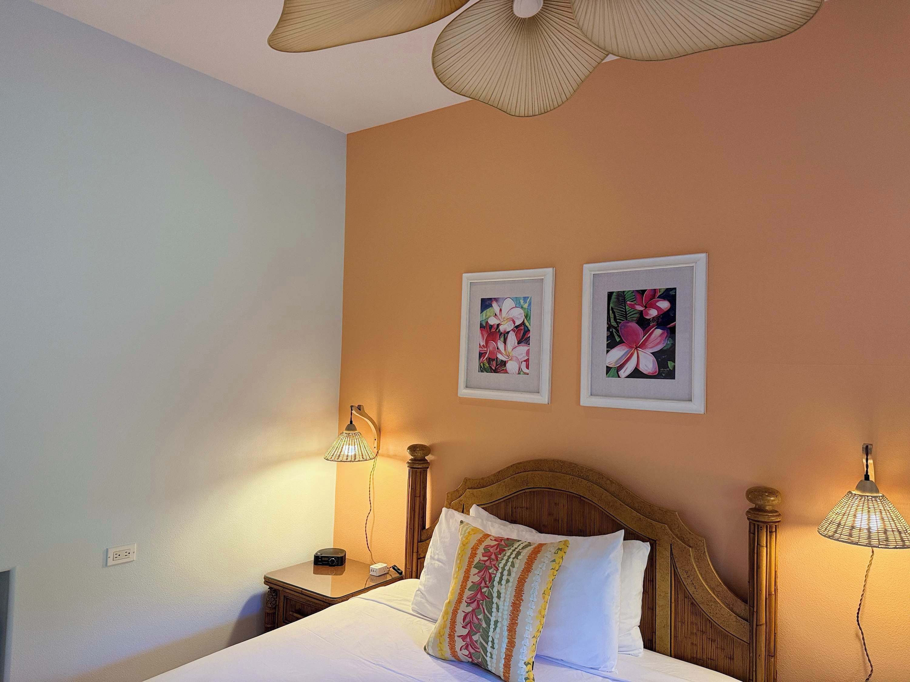 Quarto com cama, duas luminárias fixadas na parede e duas imagens de flores emolduradas.