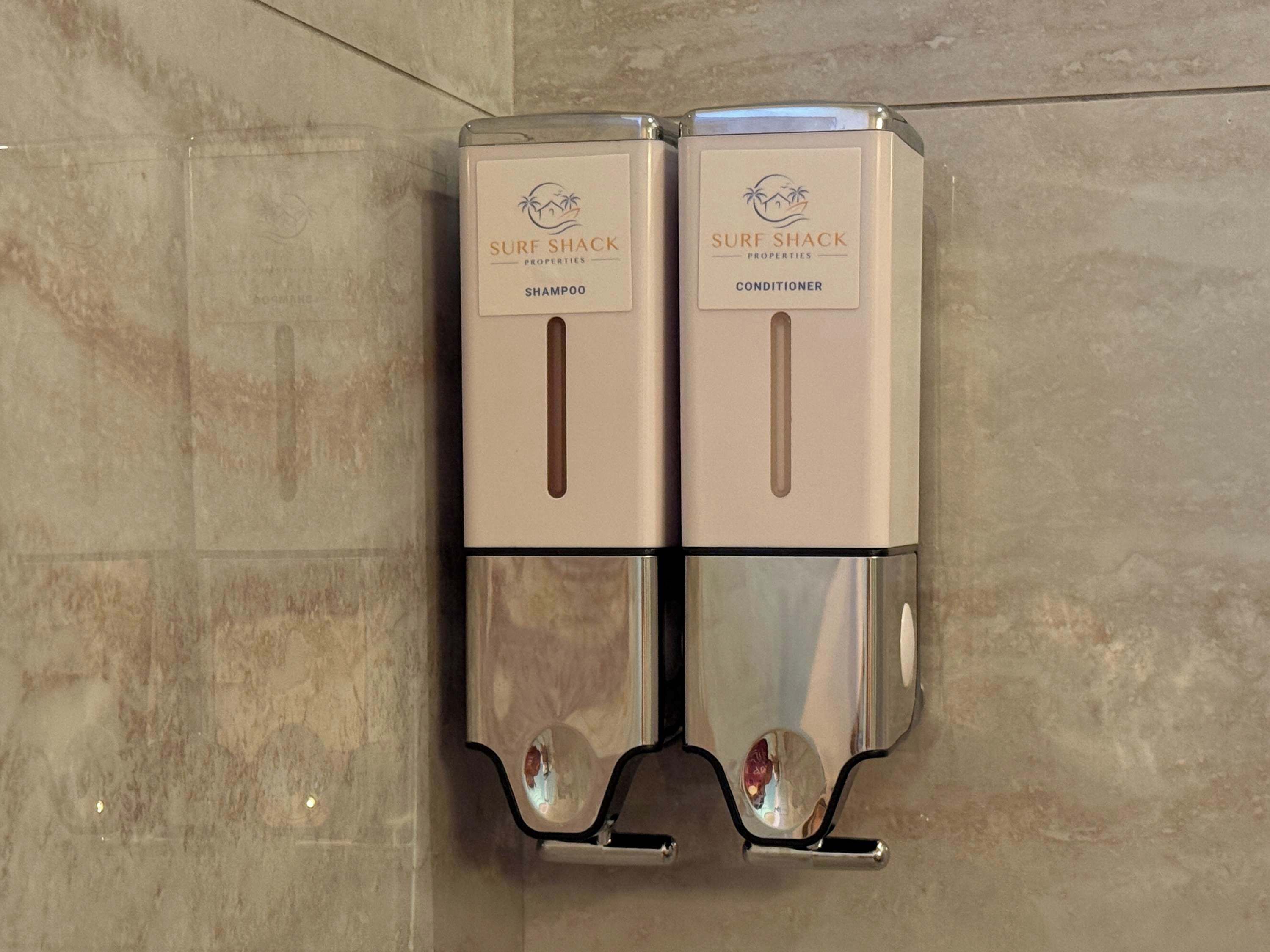 Two self-service dispensers for shampoo and conditioner at a hotel.