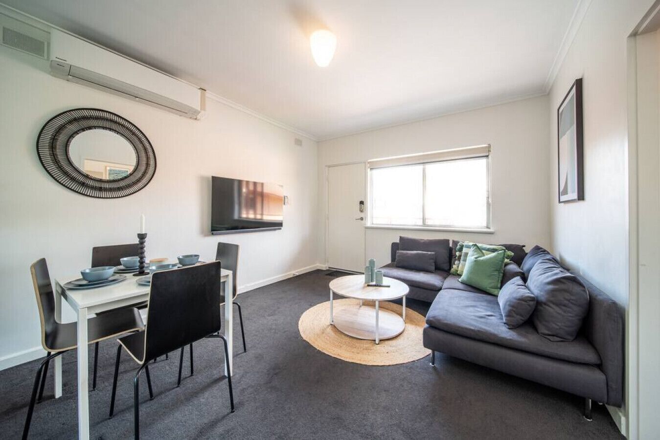 A modern living room with a dining area, a sofa, a coffee table, and a TV mounted on the wall.