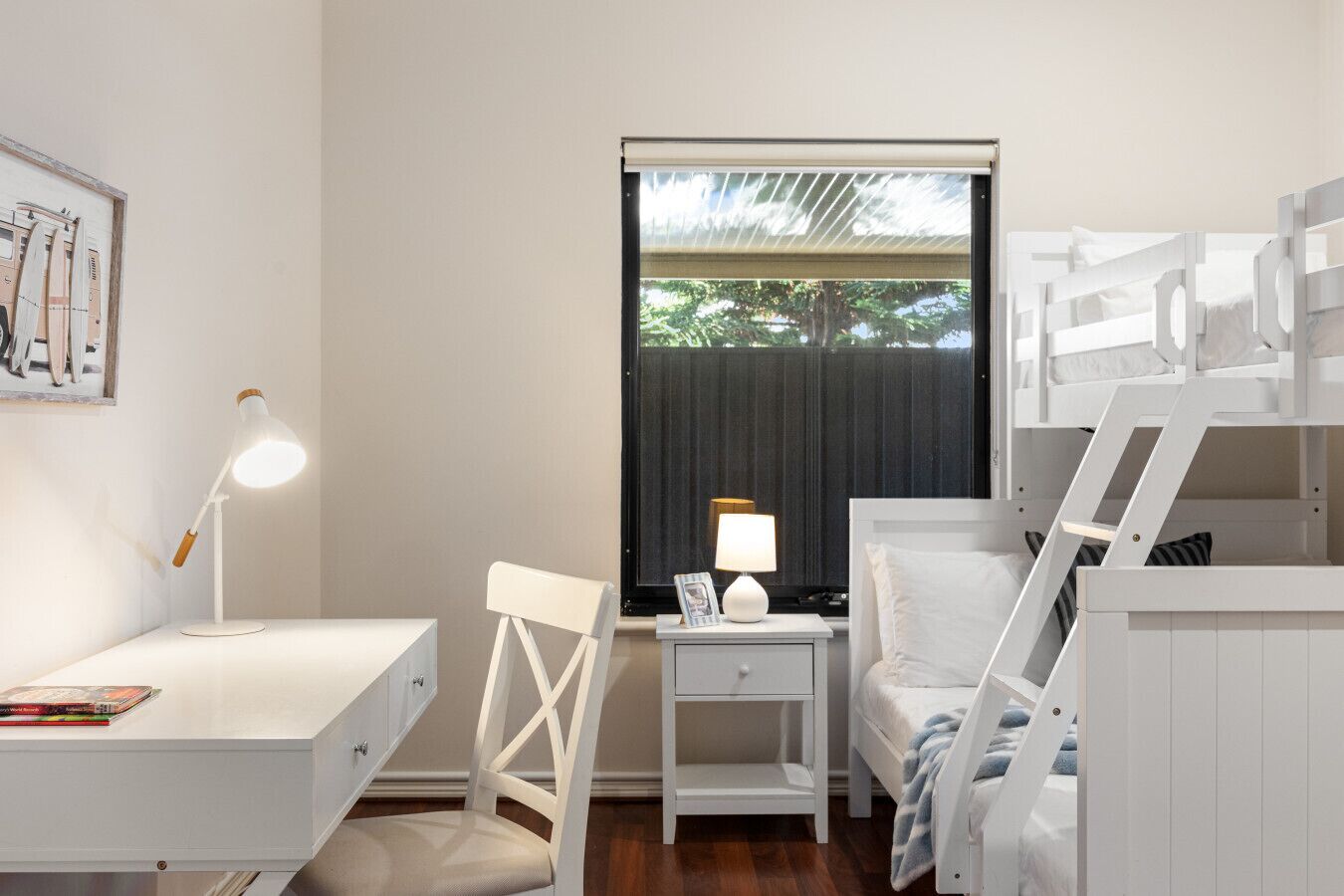 A bedroom with bunk beds, a desk with a lamp, a chair, and a bedside table with a lamp.