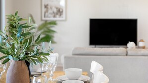 Une table à manger dressée avec des bols et des assiettes blancs, un vase contenant des feuilles vertes et une plante en pot.