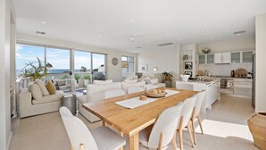 A spacious living area with a wooden dining table, white sofas, and a view of the sea.