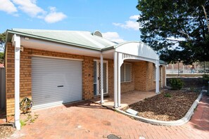 Une maison de plain-pied avec un garage, une véranda et une allée pavée en briques.