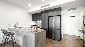 A modern kitchen with a central island, dark cabinetry, and a stainless steel refrigerator.