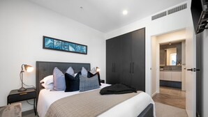 A modern bedroom with a large bed, a nightstand with a lamp, a wardrobe, and a bathroom visible through an open door.