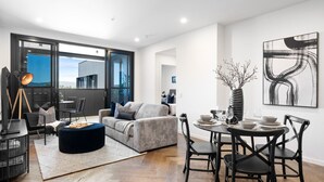 A modern living room with a grey sofa, black chairs, a round dining table set for four, and a large abstract painting on the wall.