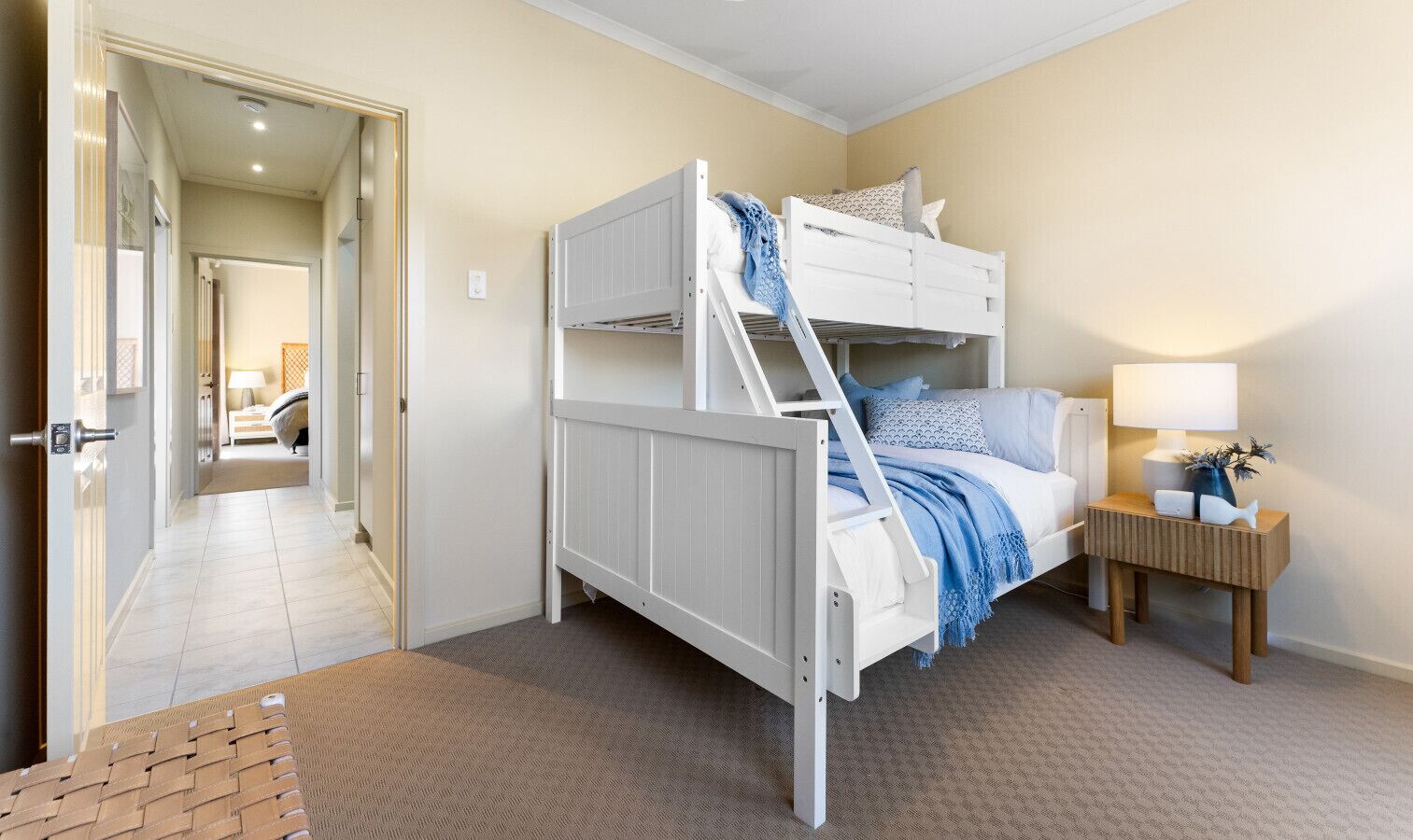 Una cama individual en un dormitorio con suelo alfombrado, una mesita de noche con lámpara y una puerta que da a otra habitación.