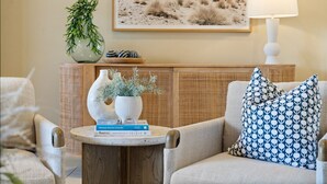 A cozy living room with a sofa, a side table with books, a lamp, and decorative vases.