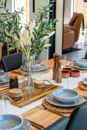 A dining table set with plates, bowls, and a vase with greenery. - Marble @ South Plympton: Effortless Family Comfort (South Plympton)
